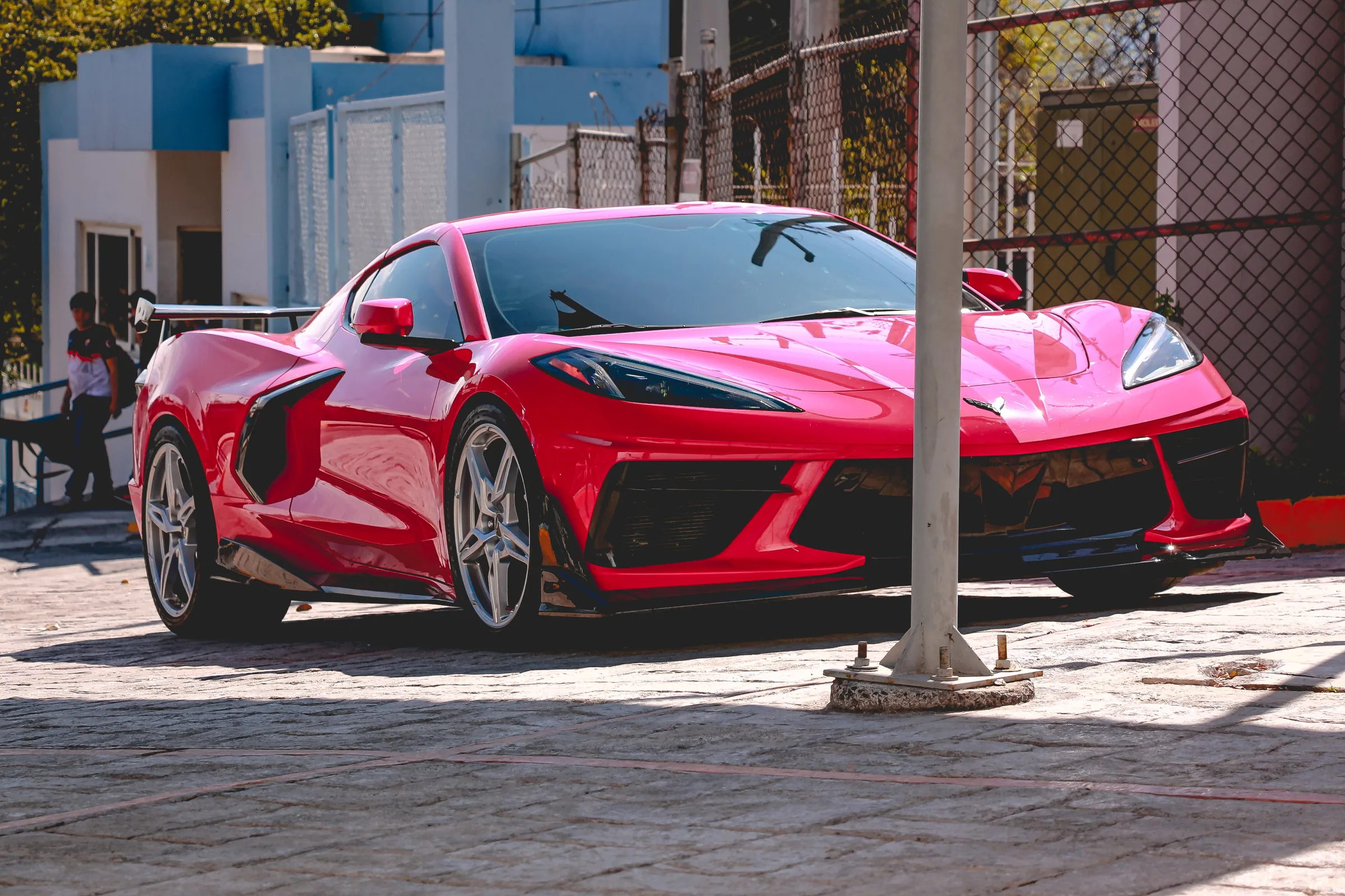 El Corvette C8 rojo de frente, con el alerón visible y una reja al fondo