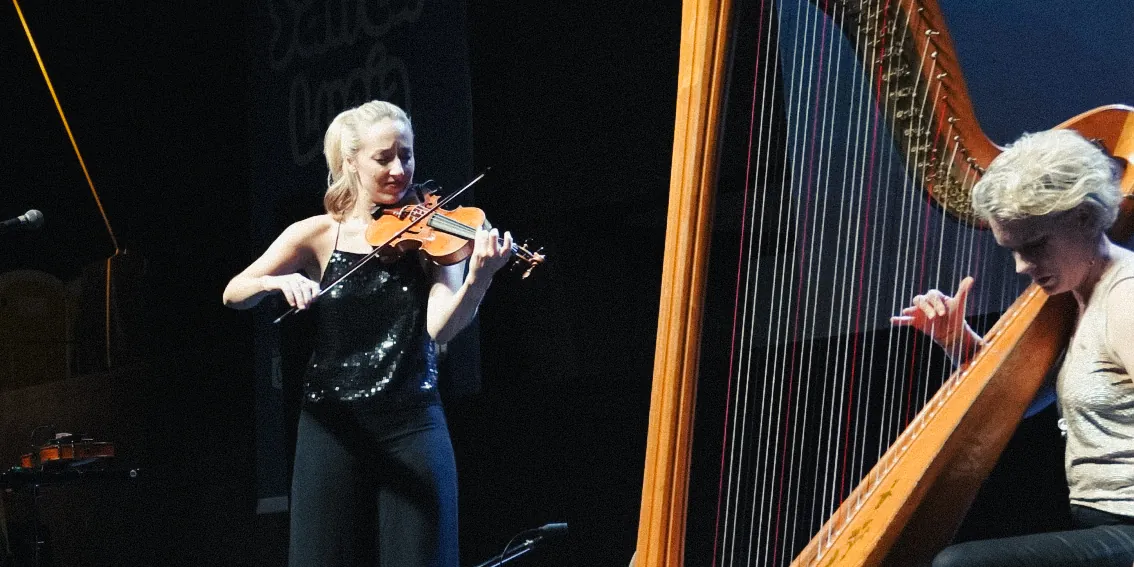 La violinista toca de pie junto al arpa
