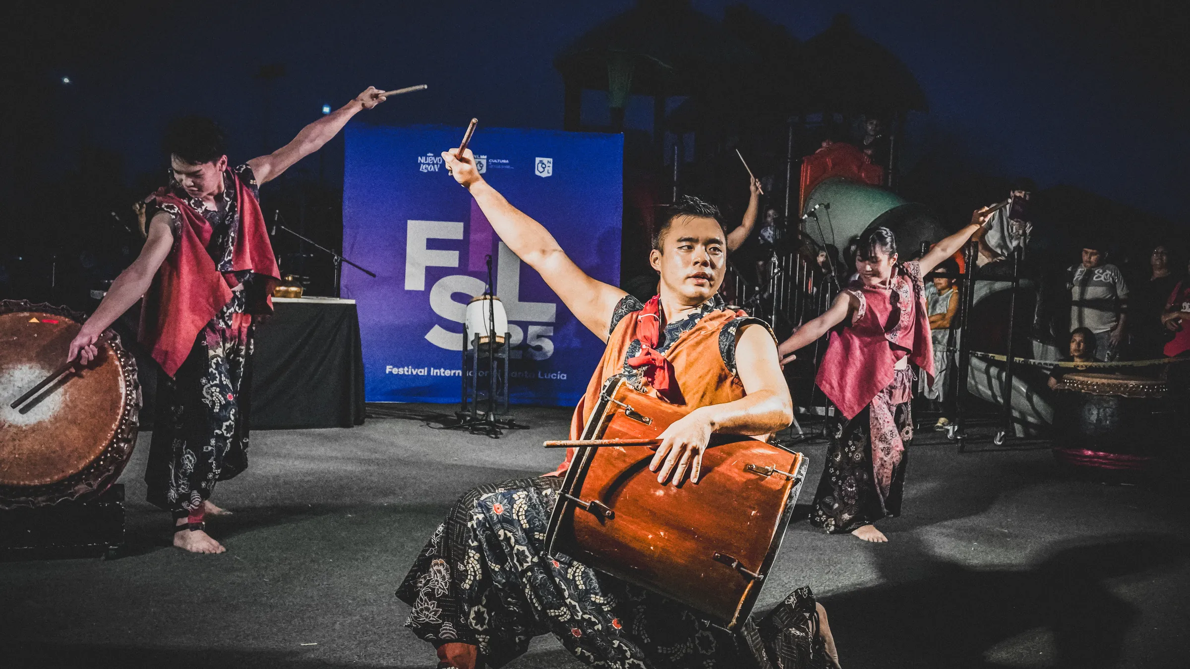 Un percusionista sonríe mientras toca, con los bailarines detrás