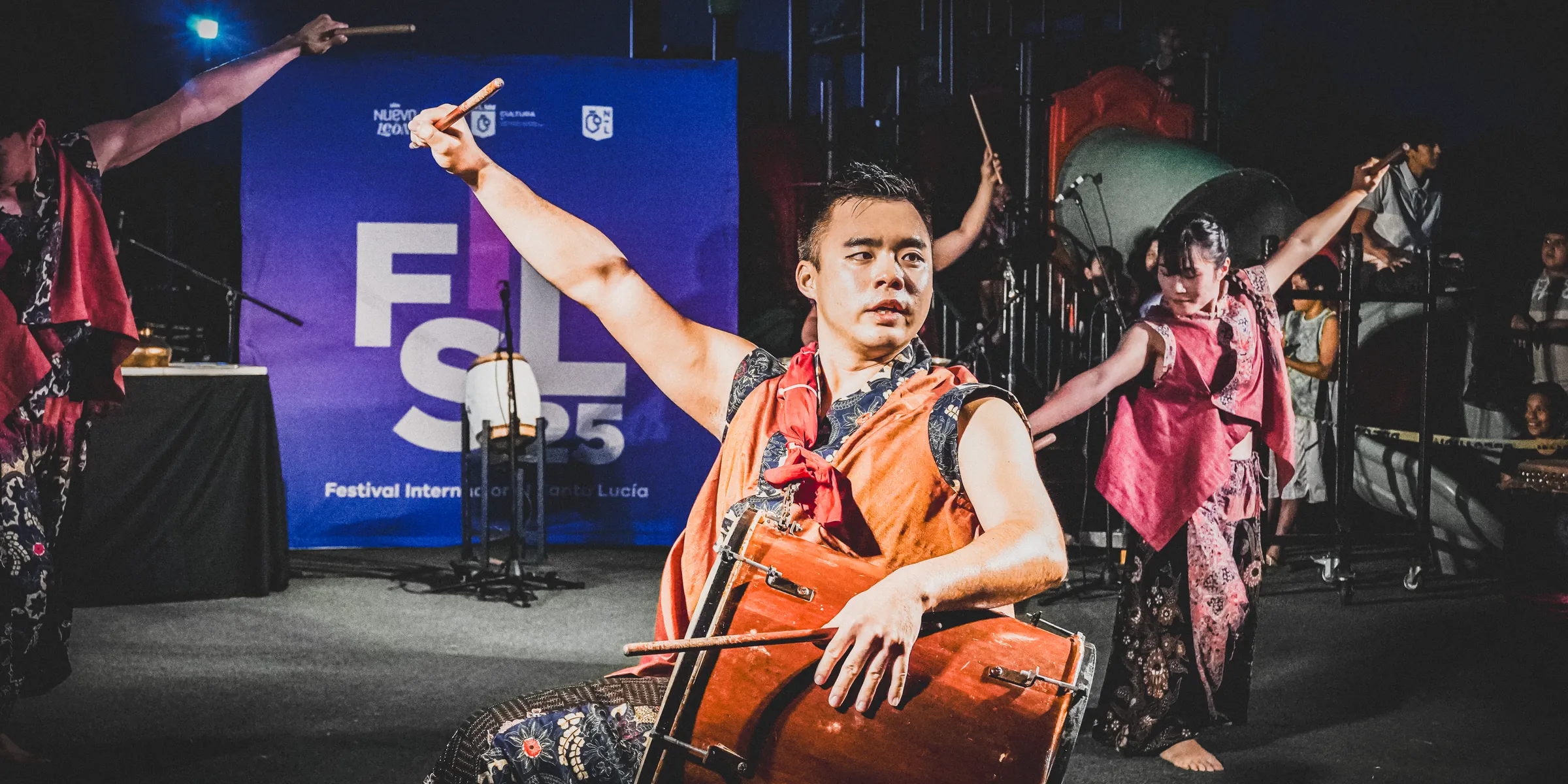 Un percusionista levanta la baqueta frente al logo del festival