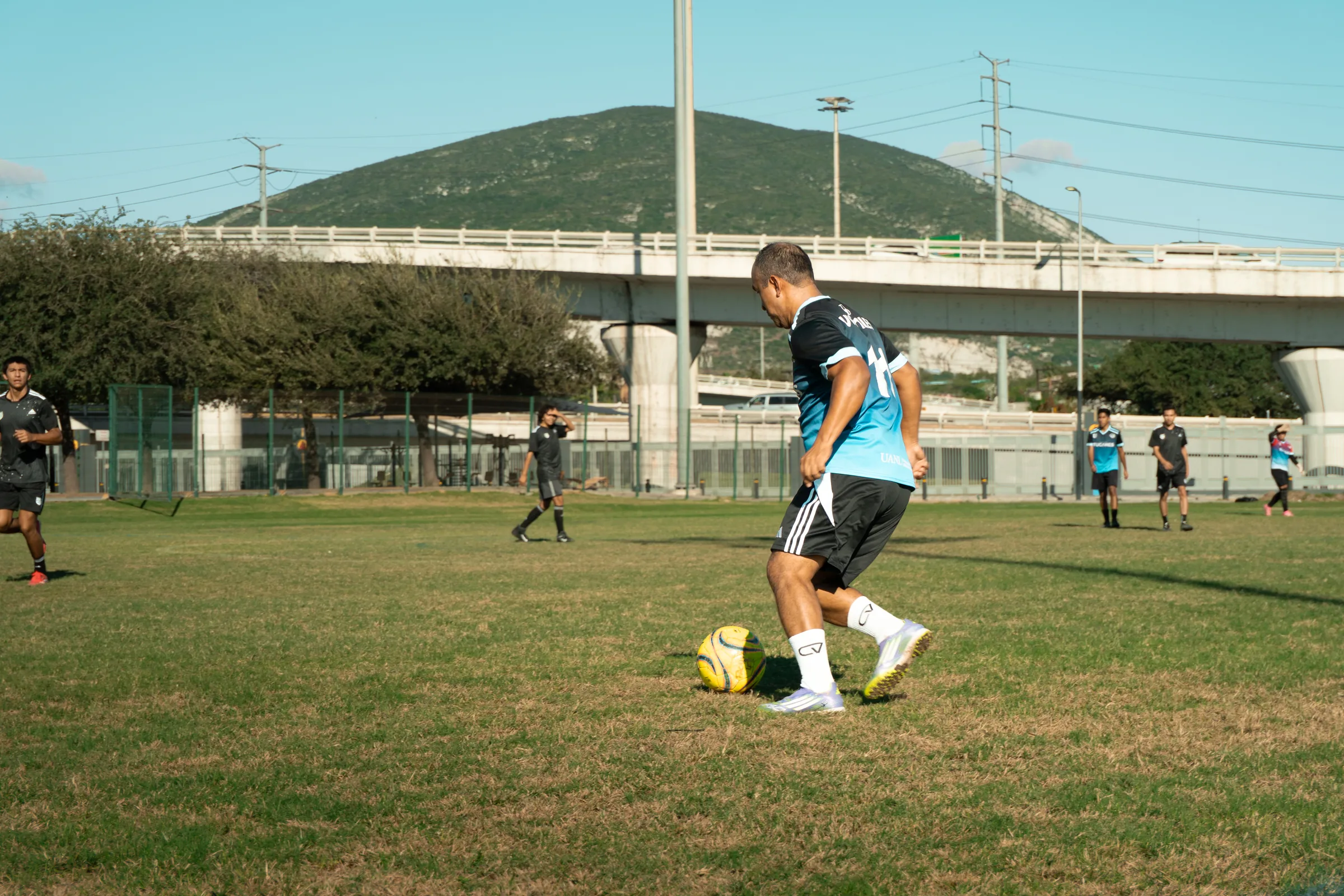 Varios jugadores corren tras el balón, con el árbitro observando y el cerro de fondo