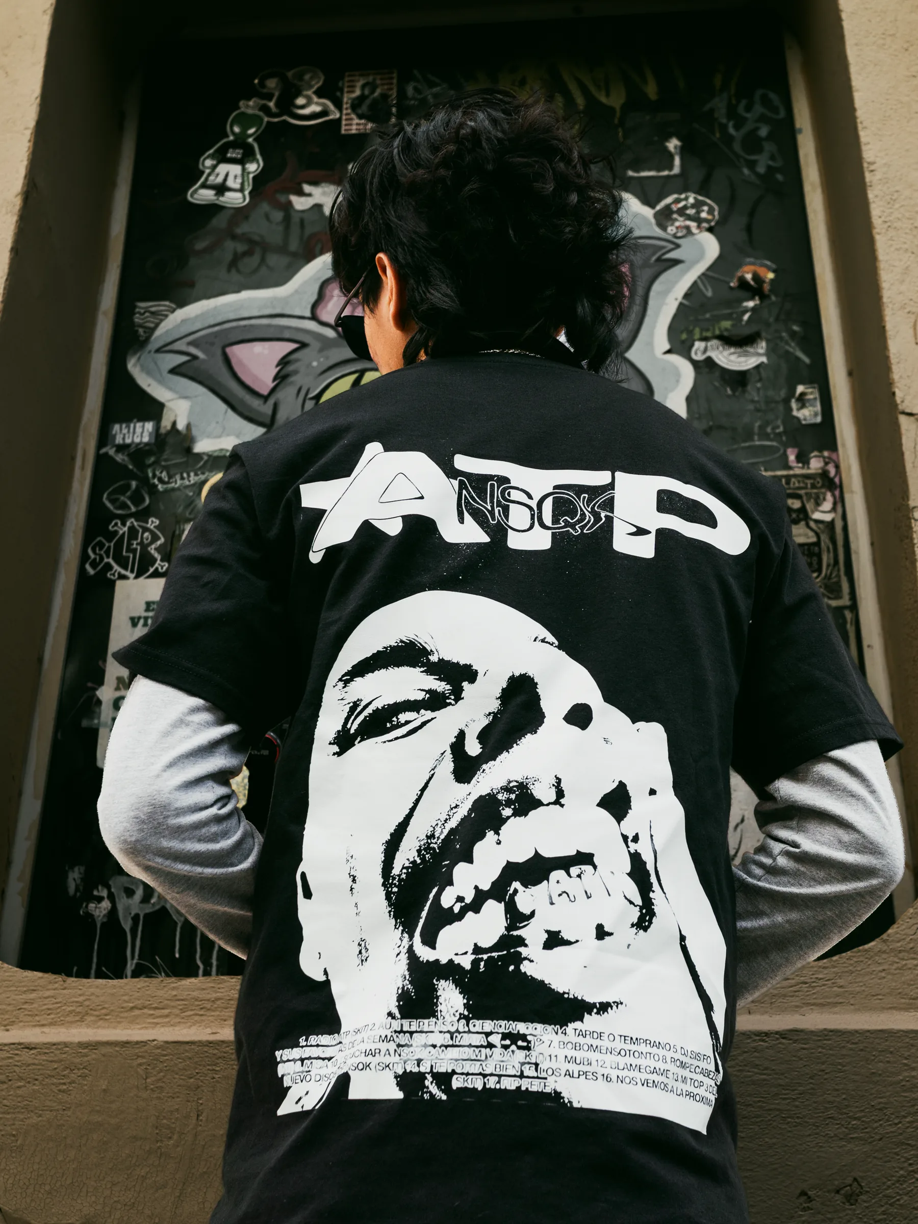 Toma cerrada de la playera ATP desde arriba, frente a la puerta con grafiti y stickers