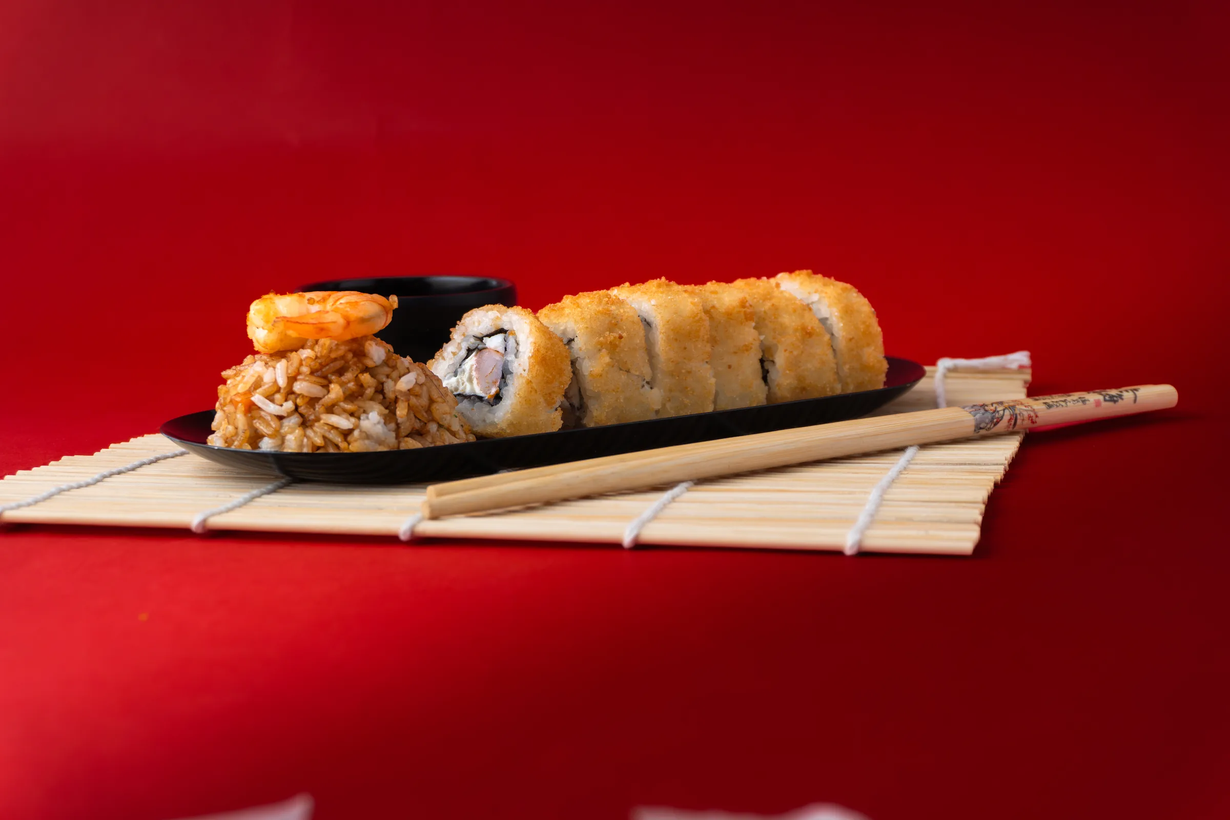 El roll empanizado en un plato negro, con el camarón sobre el arroz y la salsa a un lado