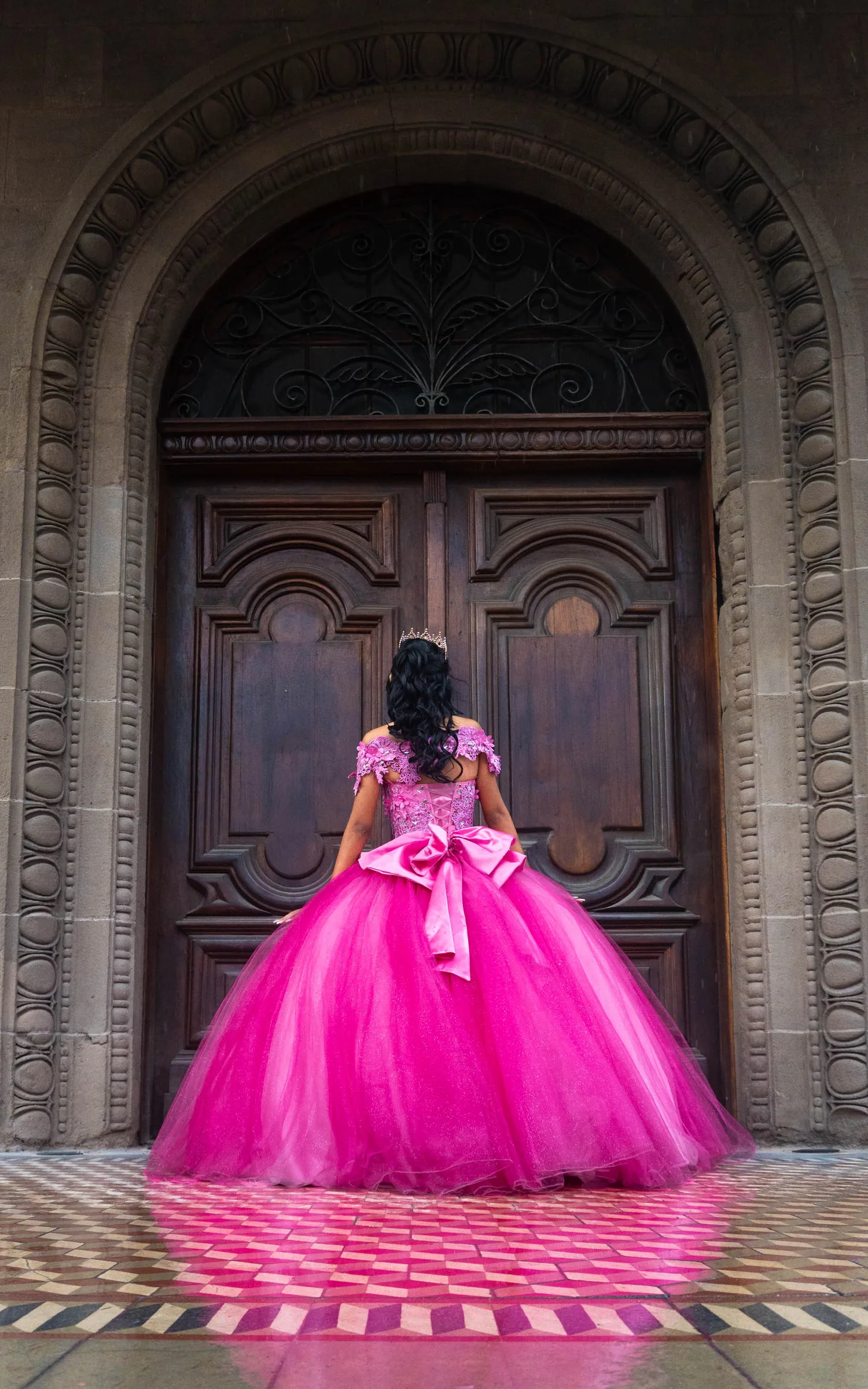 Arleth de espaldas frente a la puerta de madera con arco, con el moño del vestido al centro